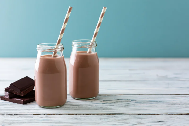 Two glass bottles of chocolate milk with striped straws on a wooden table