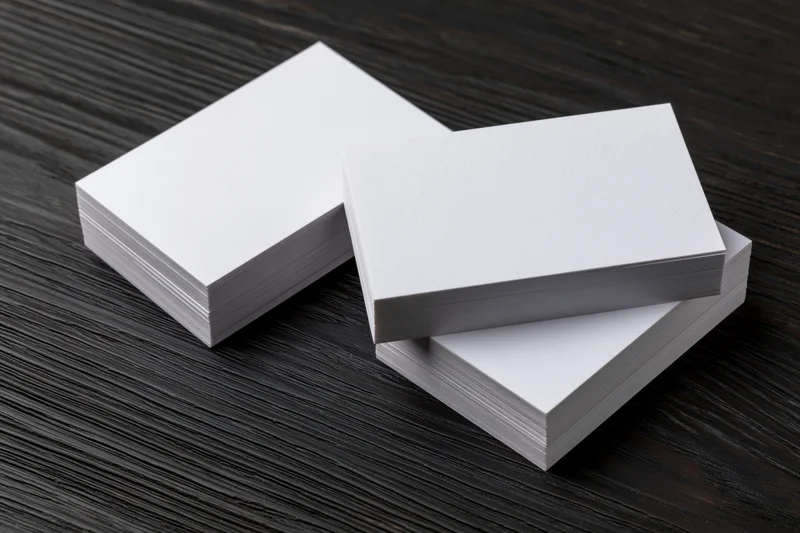 Two stacks of blank white business cards arranged on dark wooden surface