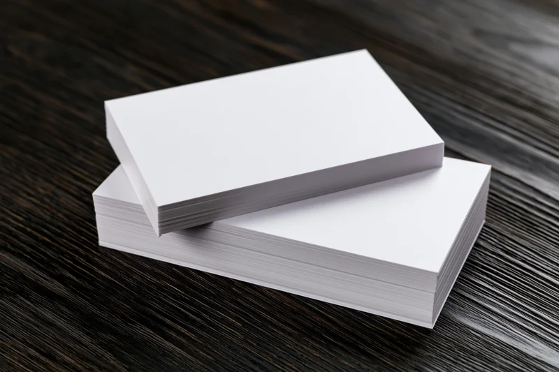 Two stacks of blank white business cards arranged on a dark wooden table
