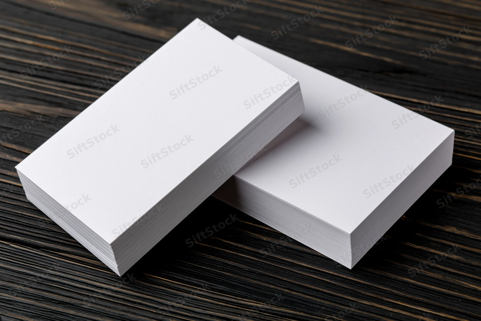 Two stacks of blank white business cards arranged on dark wooden surface