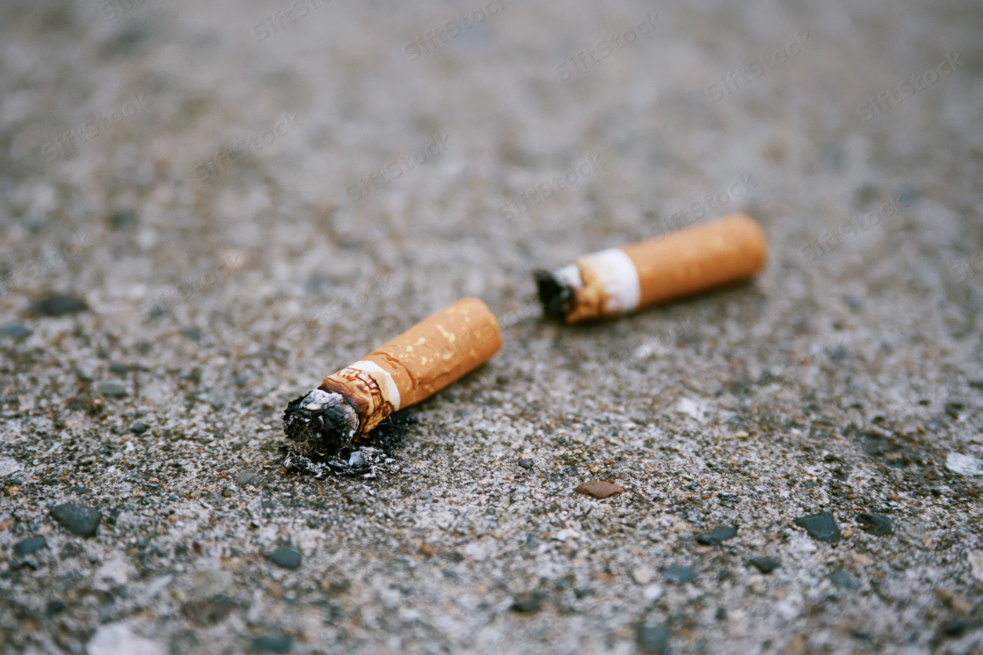 Two stubbed-out cigarette butts lying on rough concrete pavement