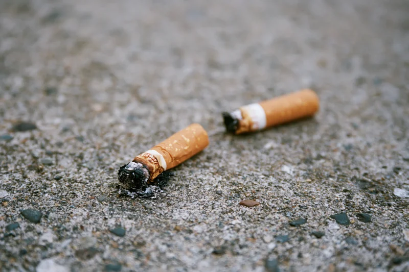 Two stubbed-out cigarette butts lying on rough concrete pavement