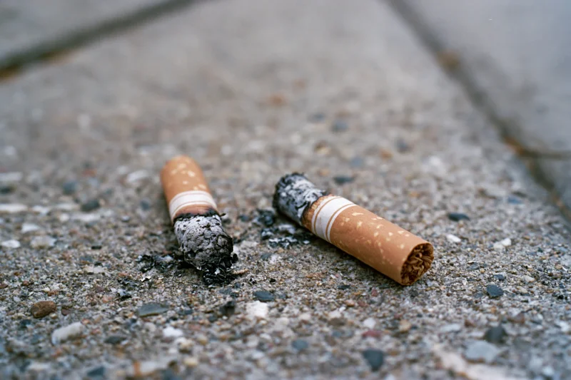 Two smoked cigarette butts lying on rough concrete pavement
