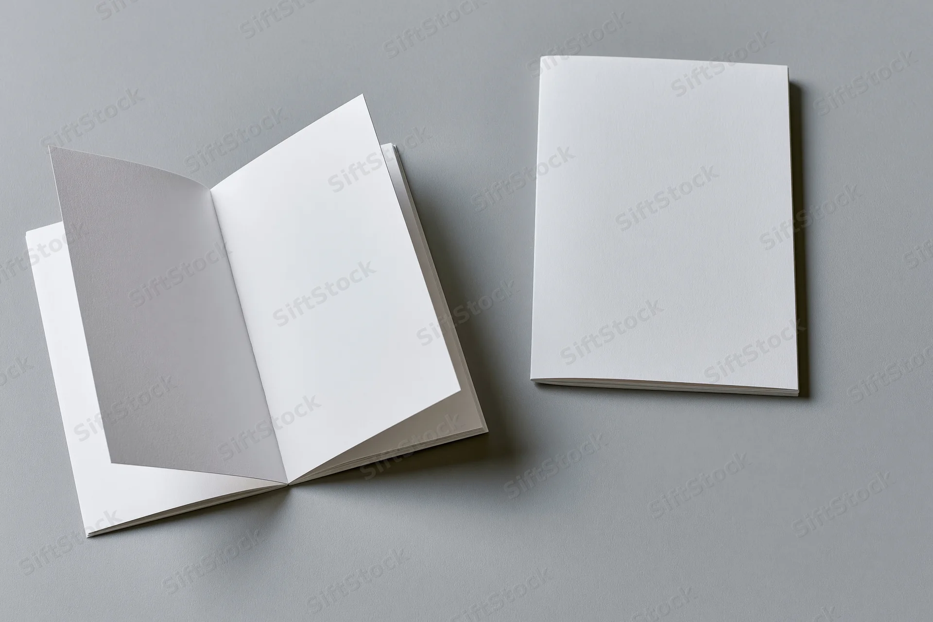 Two blank white booklets one open and one closed on a flat grey surface