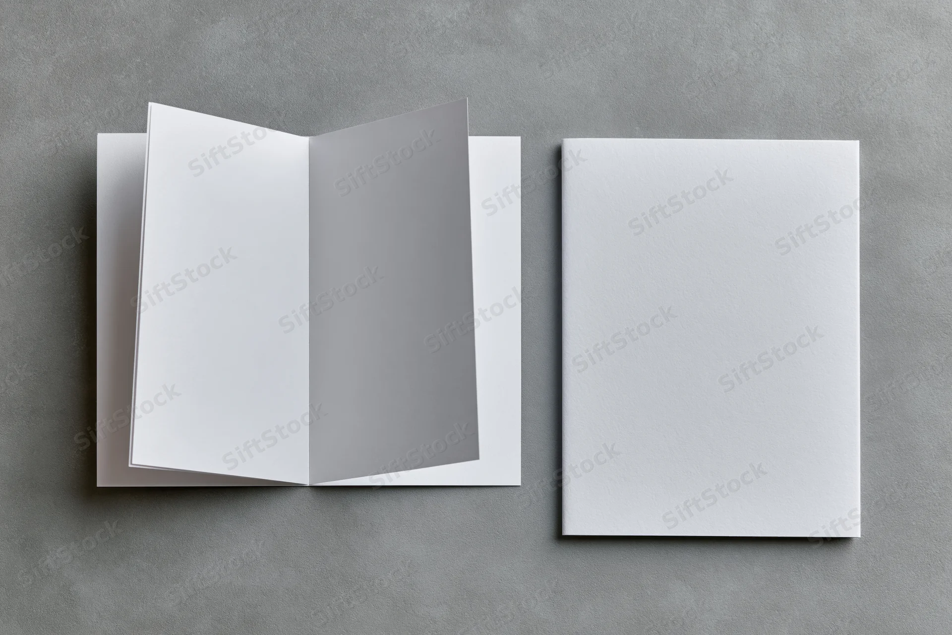 Two blank white booklets one open and one closed on a flat gray surface
