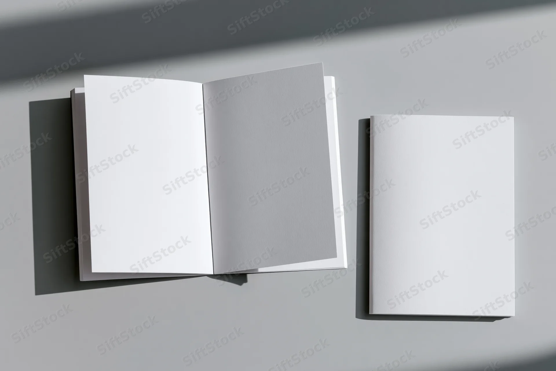 Two white blank booklets one open and one closed on a flat gray surface