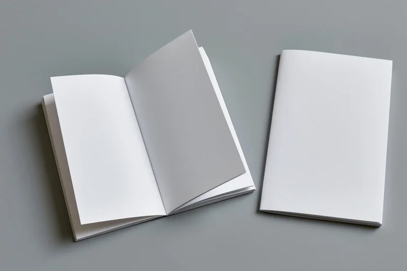 Two white blank booklets one open and one closed on a flat gray surface