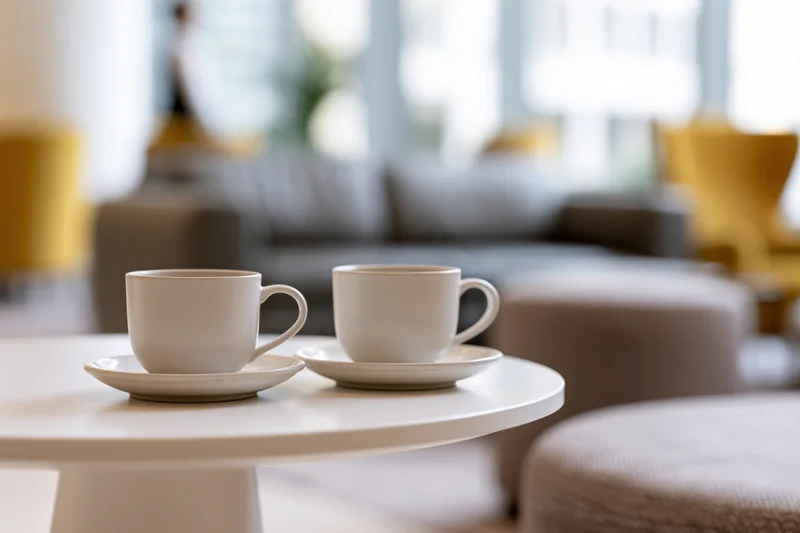 Two white ceramic coffee cups on saucers on a round table in a modern living room