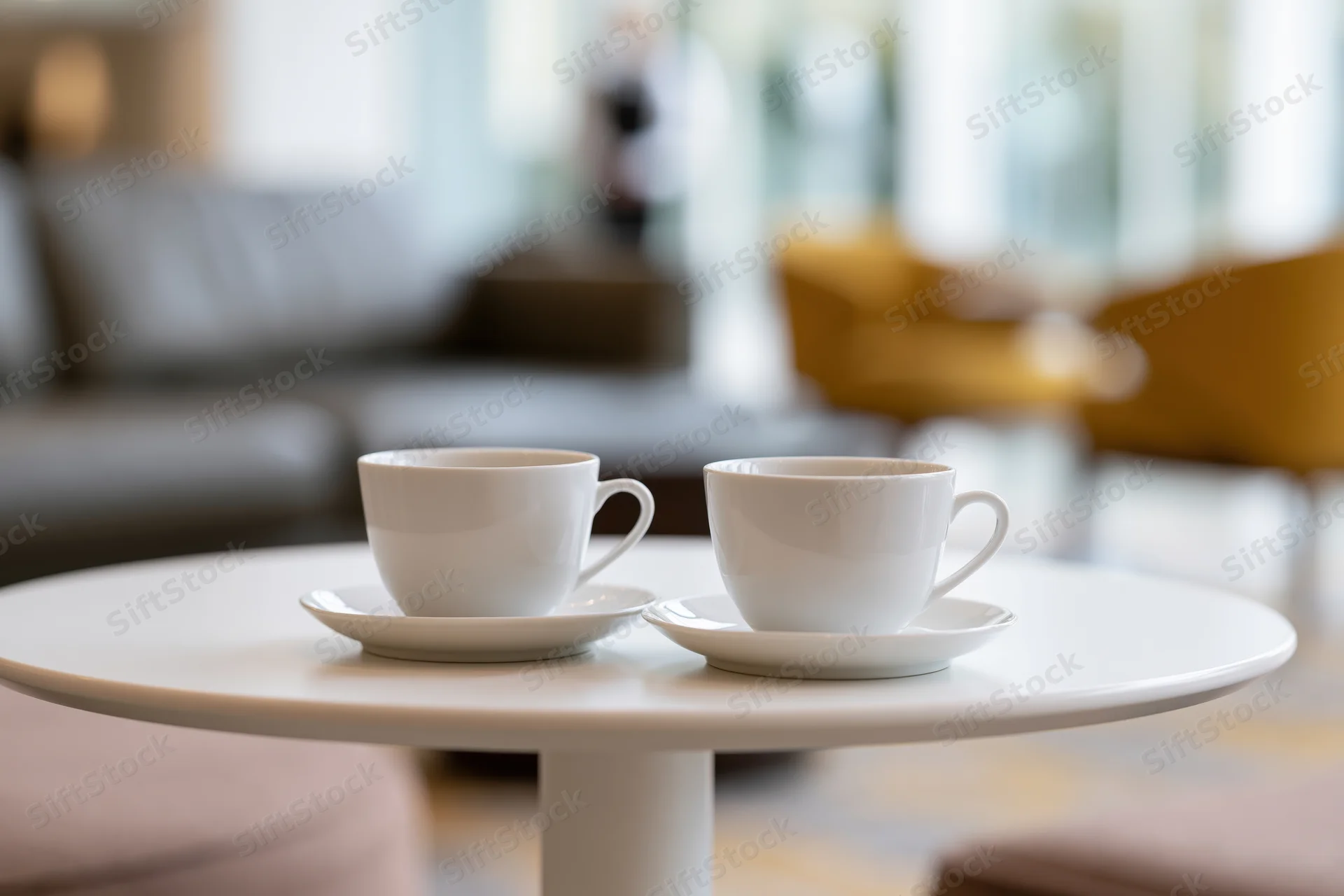 Two white ceramic coffee cups on saucers on a round table in a modern living room