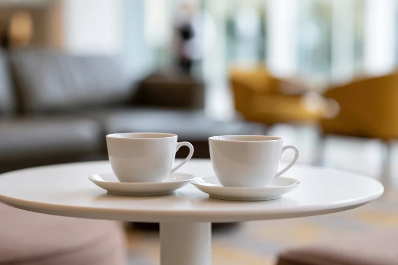 Two white ceramic coffee cups on saucers on a round table in a modern living room