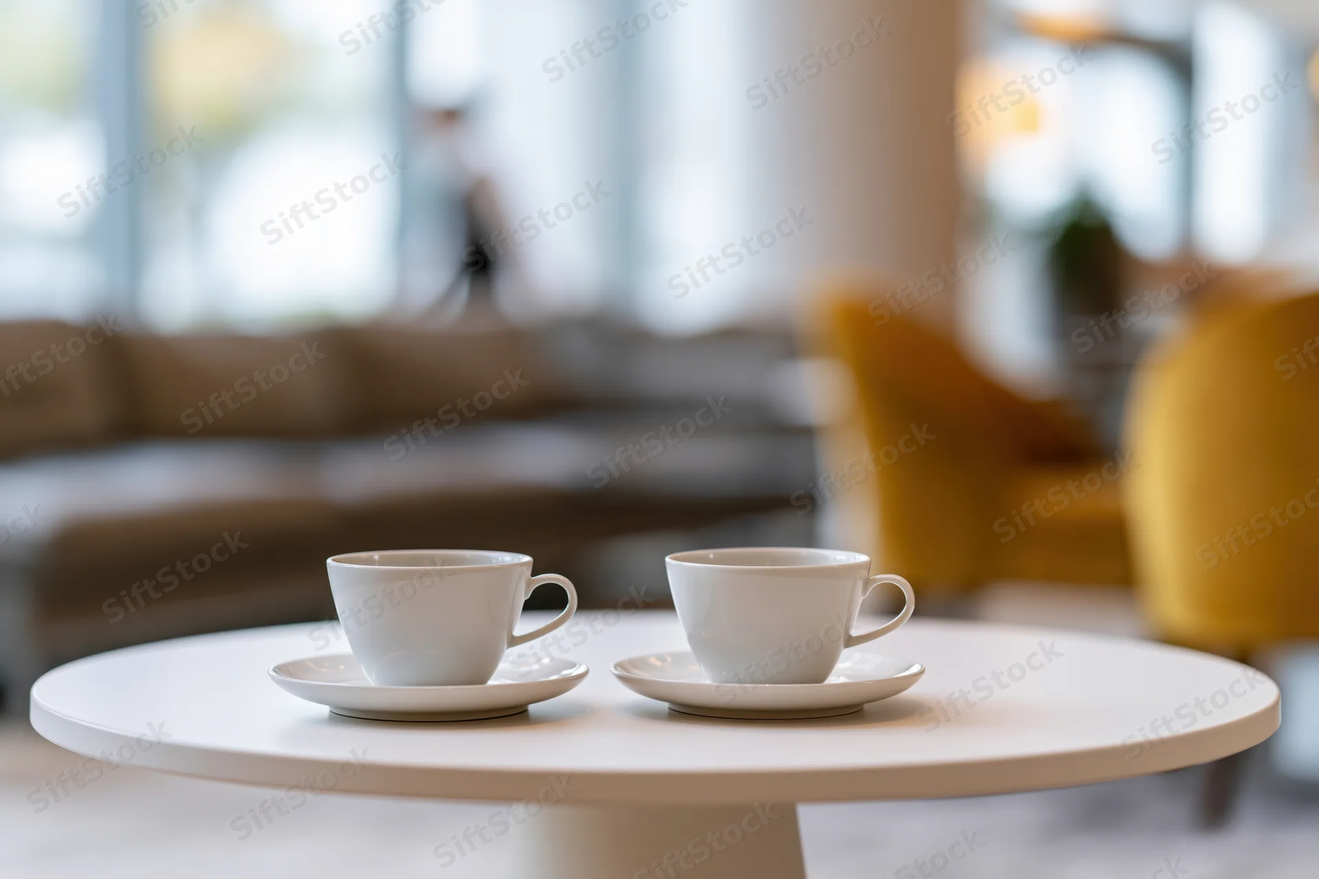 Two white ceramic coffee cups on saucers on a round table in a modern living room