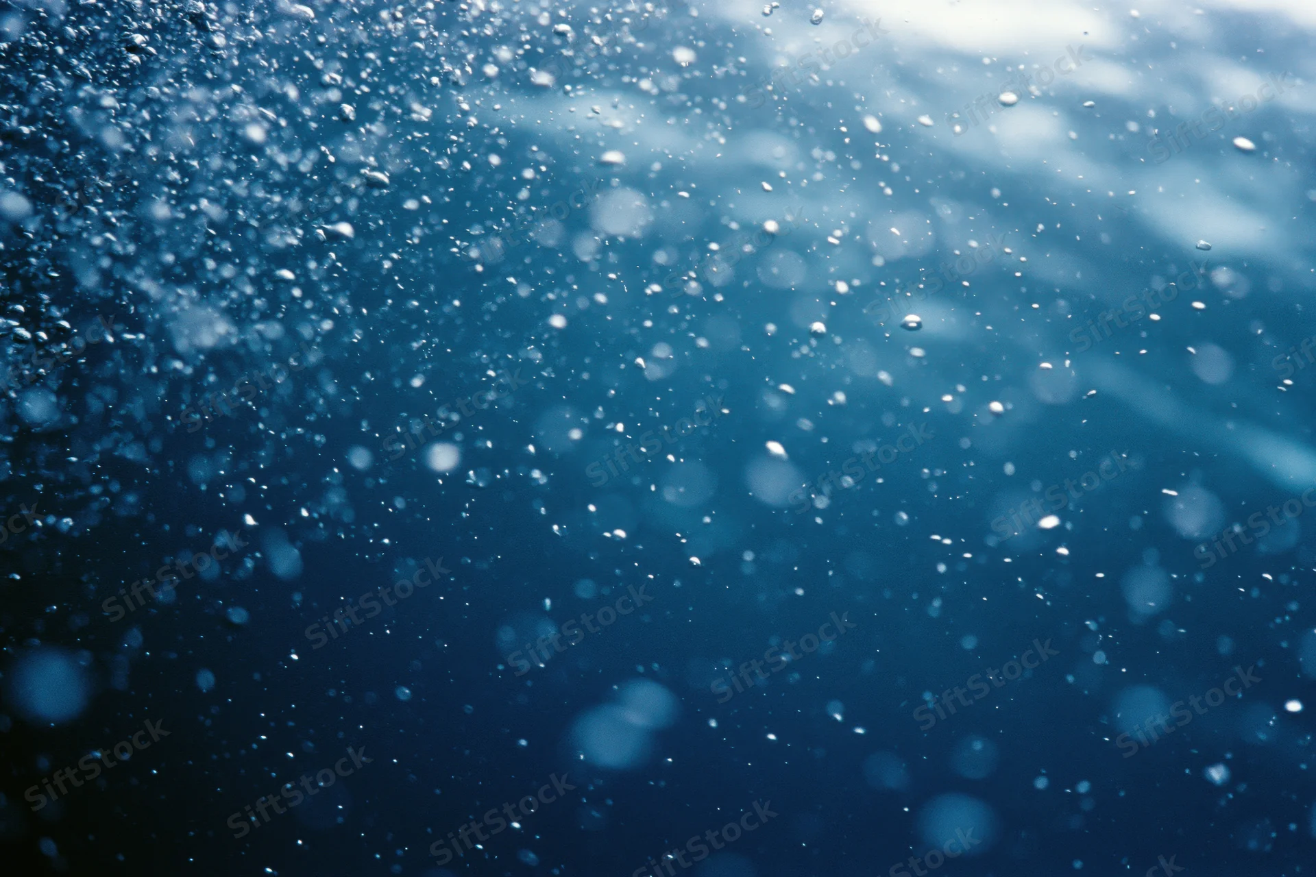 Underwater view looking up through floating bubbles toward sunlit surface in deep blue ocean