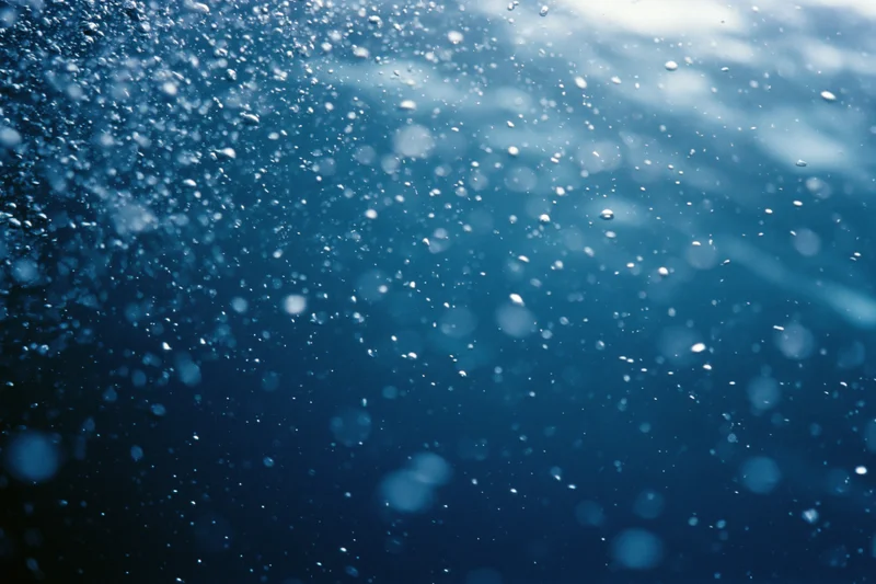 Underwater view looking up through floating bubbles toward sunlit surface in deep blue ocean
