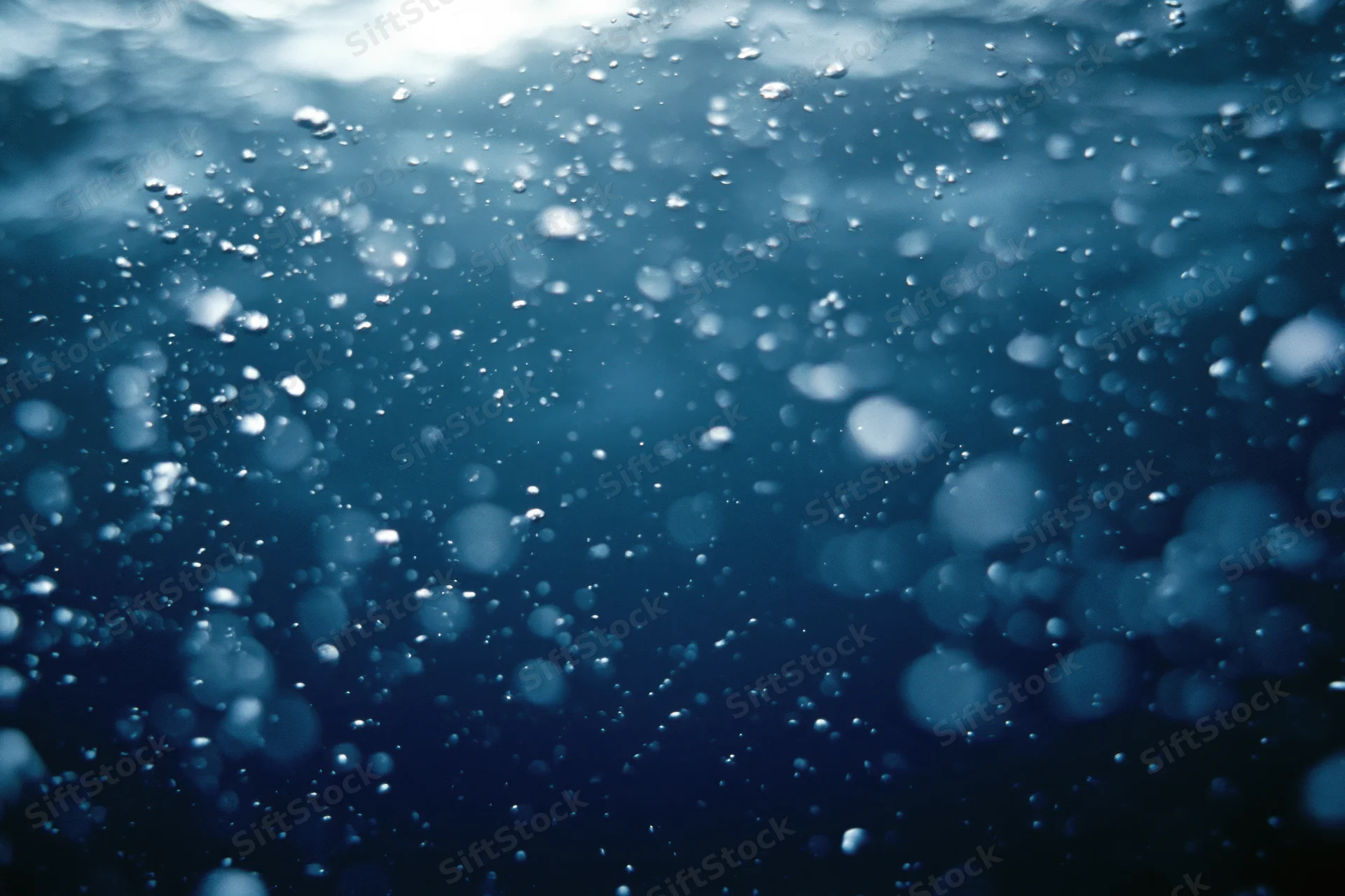 Underwater view looking up toward the surface with rising air bubbles and sunlight filtering through the water