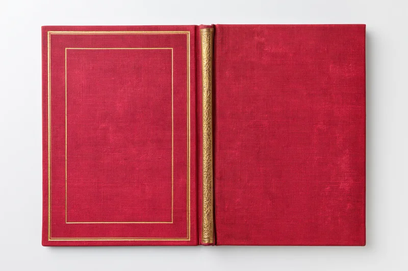 Open vintage hardcover book with red cloth covers and gold embossed frame lying flat on white background