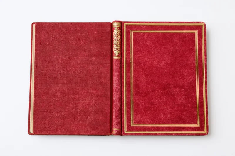 Open vintage hardcover book with red textured covers and gold embossed spine lying flat on white background