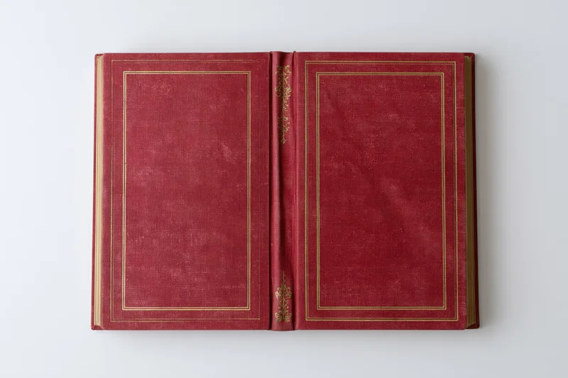 Open vintage hardcover book with red leather covers and gold embossing lying flat on white surface