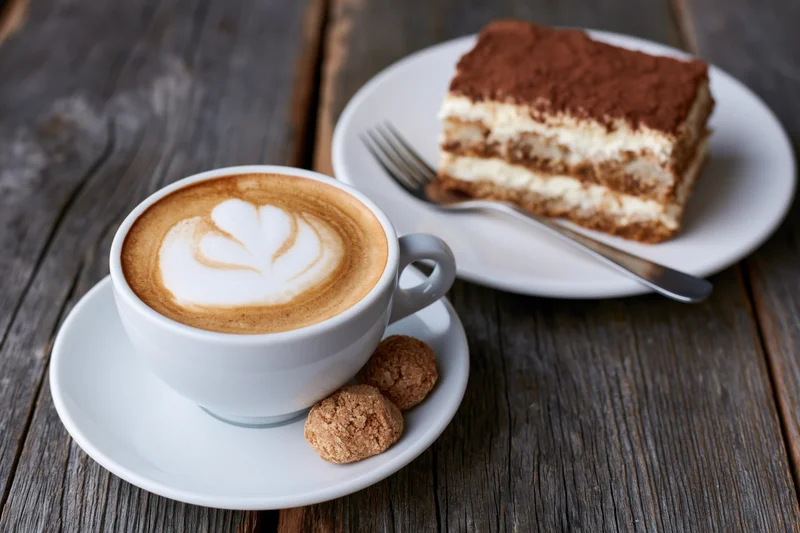 Cappuccino with heart-shaped latte art and a slice of tiramisu on a wooden table