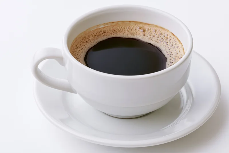 White ceramic coffee cup filled with black coffee on a saucer against a plain white background