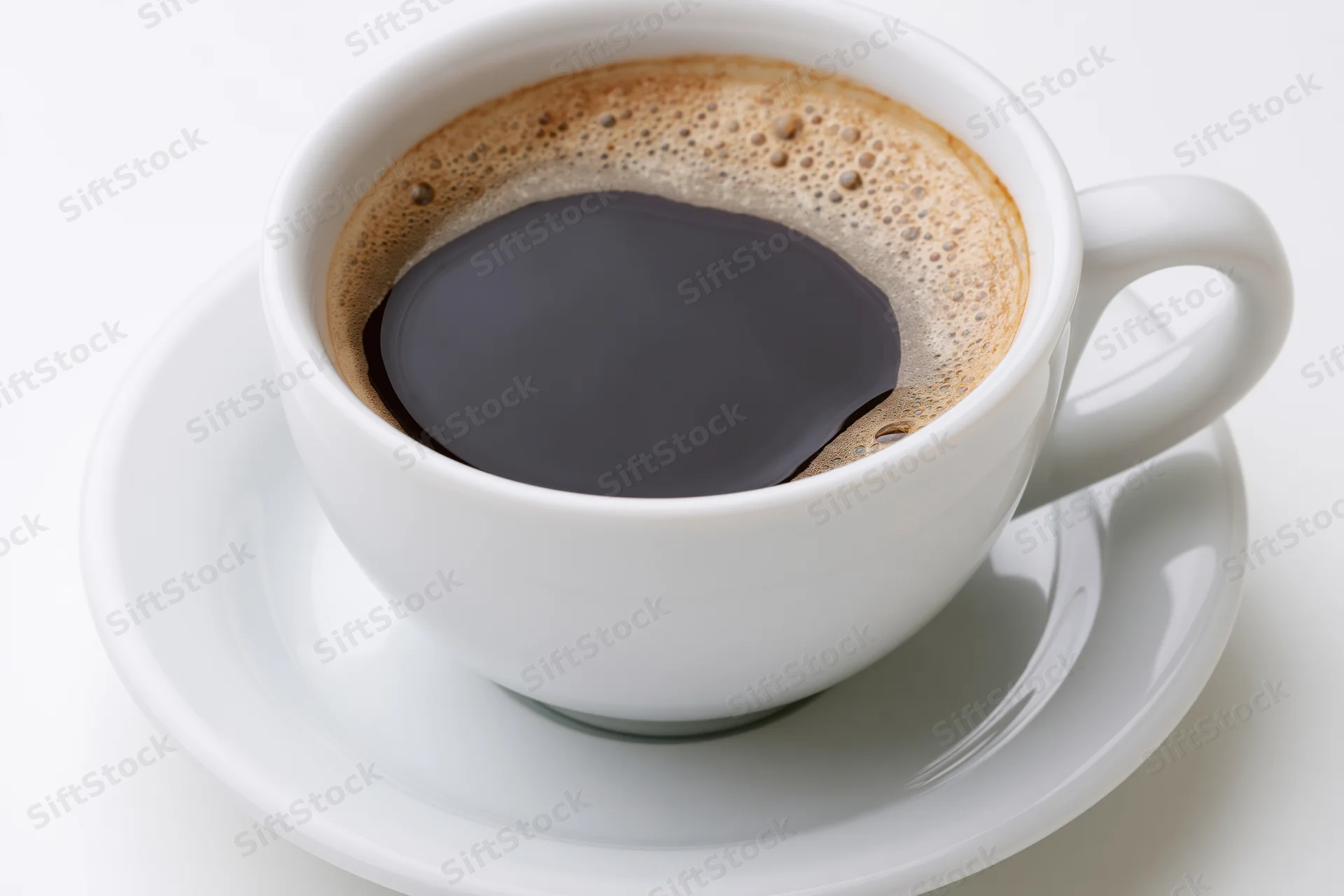 White ceramic coffee cup filled with black coffee and foam on a saucer against a white background