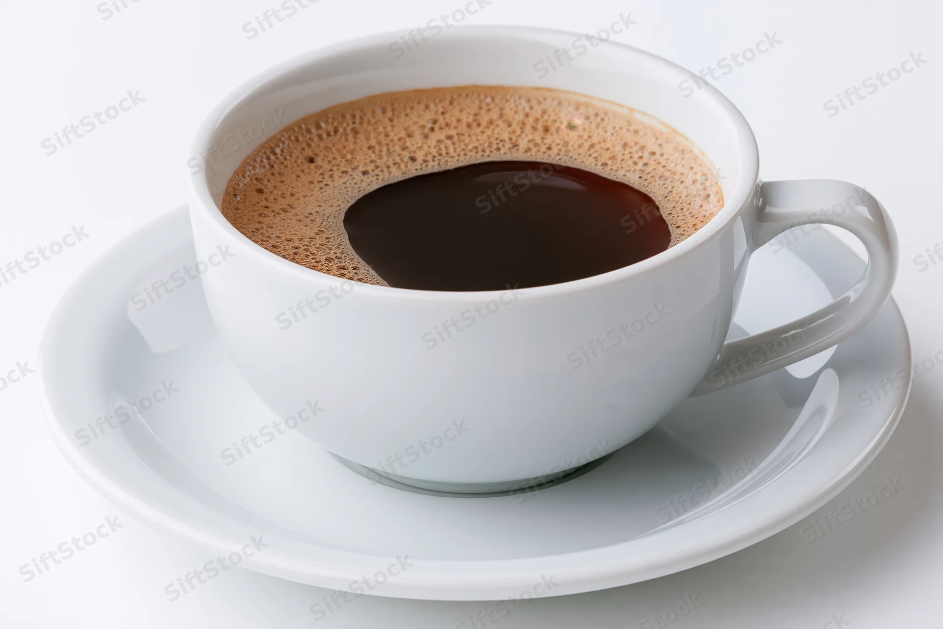 White ceramic coffee cup filled with black coffee topped with foam on a saucer against a white background
