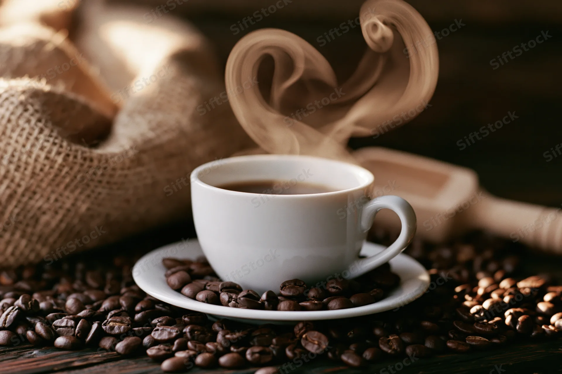 White ceramic coffee cup with heart-shaped steam on saucer surrounded by roasted coffee beans on dark wooden table
