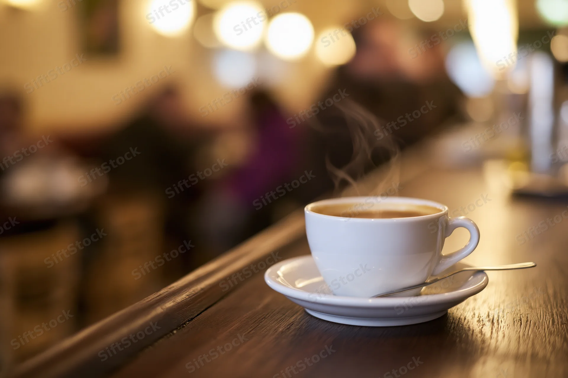 Steaming coffee cup on saucer with spoon on wooden bar in cafe interior