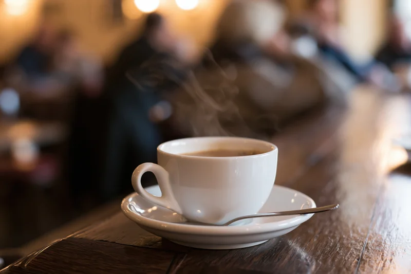 Steaming coffee cup on saucer with spoon on wooden table in cafe interior