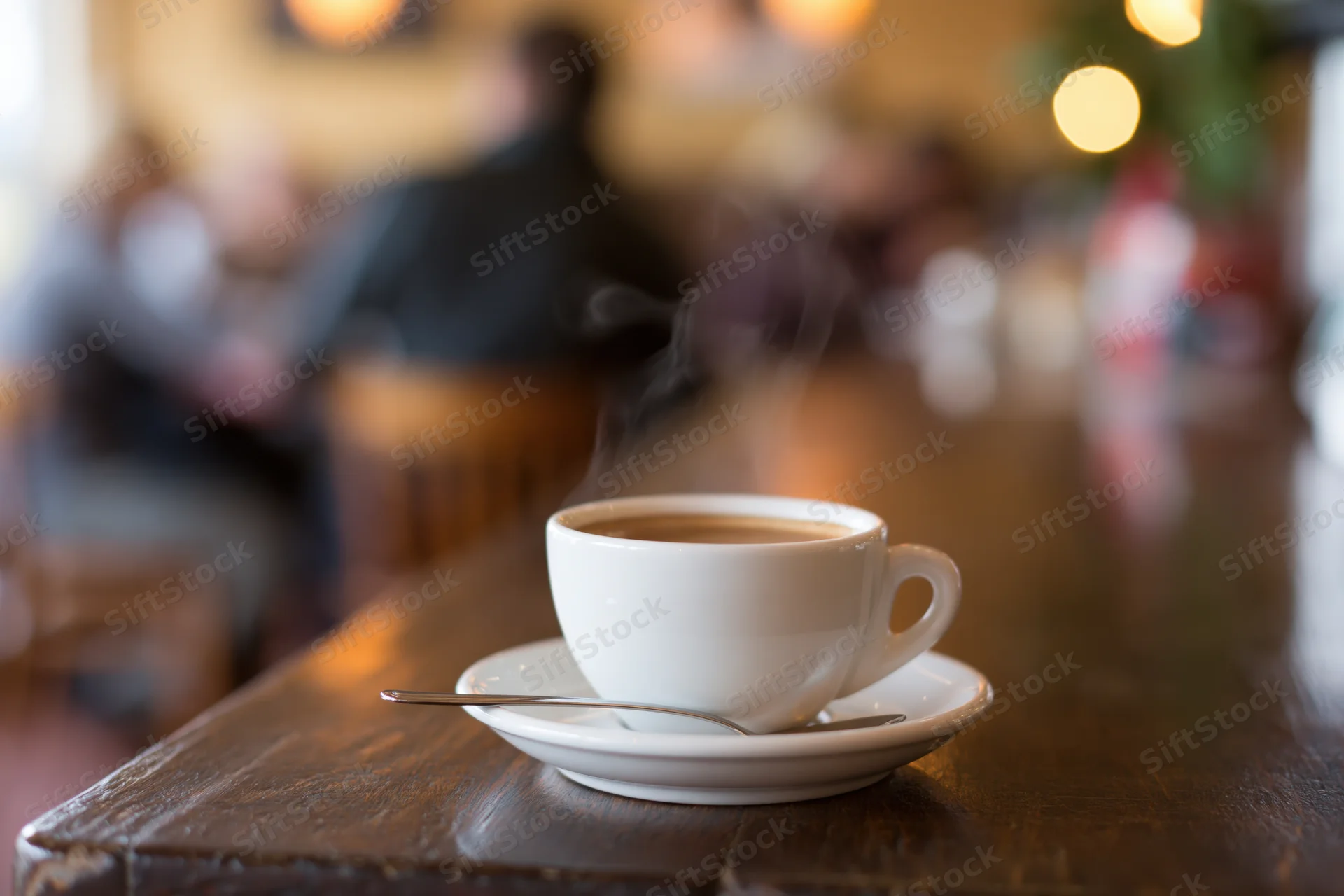 Steaming coffee cup on saucer with spoon on wooden table in cafe interior