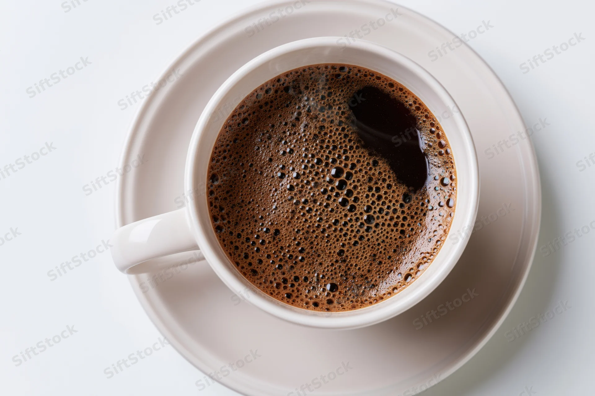 White ceramic cup of black coffee with foam on matching saucer viewed from above on plain surface