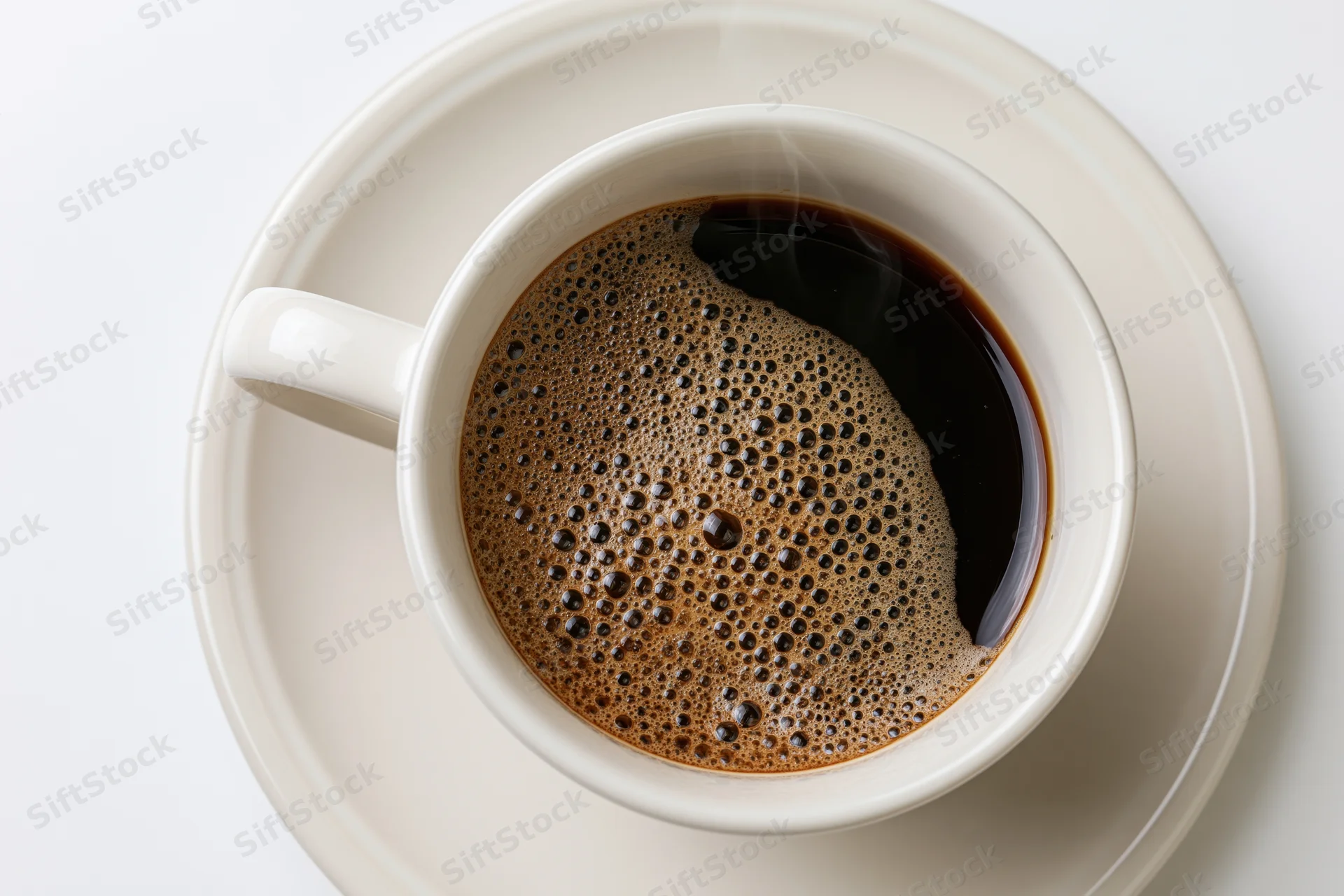 White ceramic cup of black coffee with foam and steam on matching saucer, overhead view