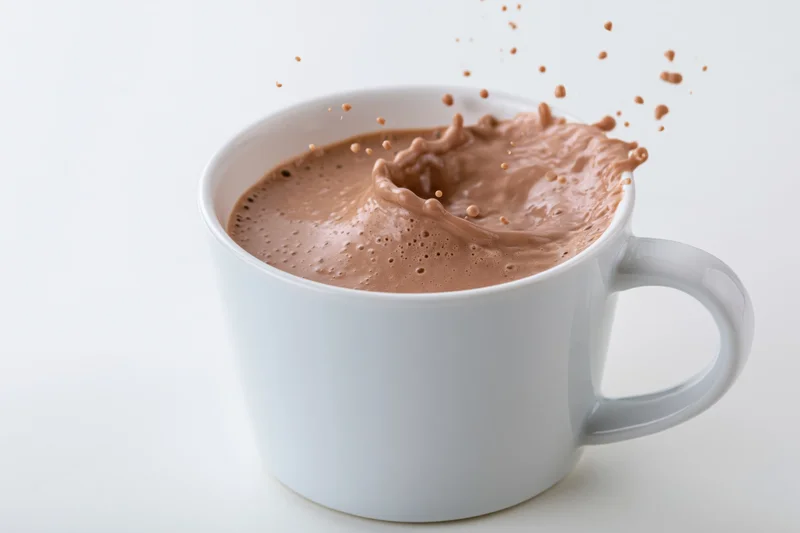 White ceramic mug filled with hot chocolate splashing against plain white background