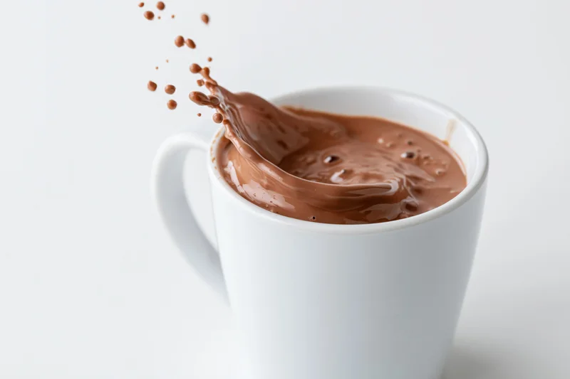 Chocolate liquid splashing from a white ceramic mug on a plain white surface