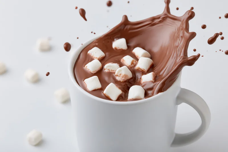 White ceramic mug filled with hot chocolate mid-splash with marshmallows floating on surface