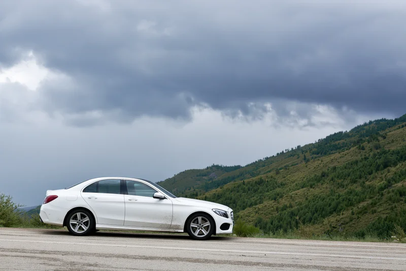 White sedan parked on mountain road shoulder under cloudy sky