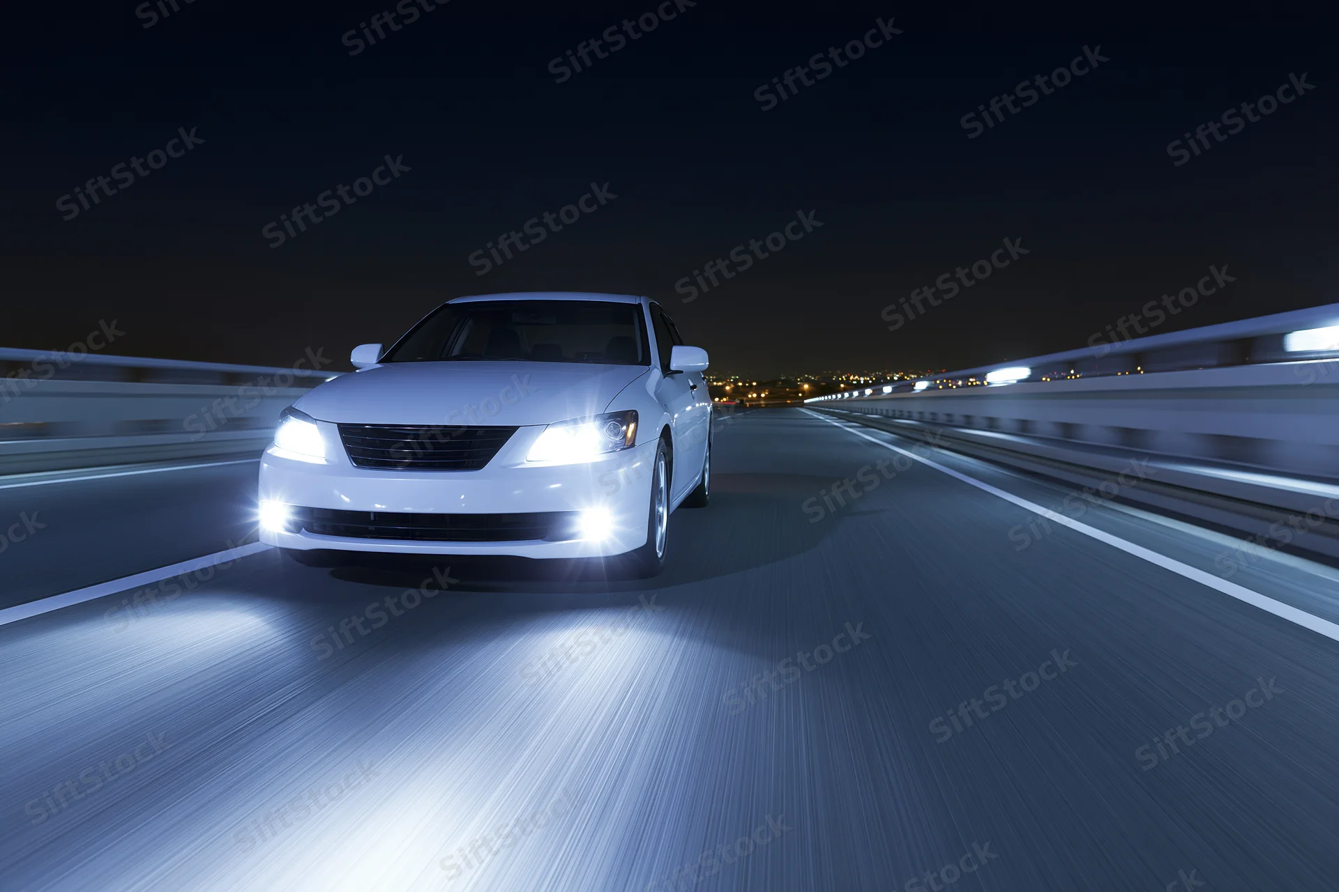 White sedan driving at speed on elevated highway at night