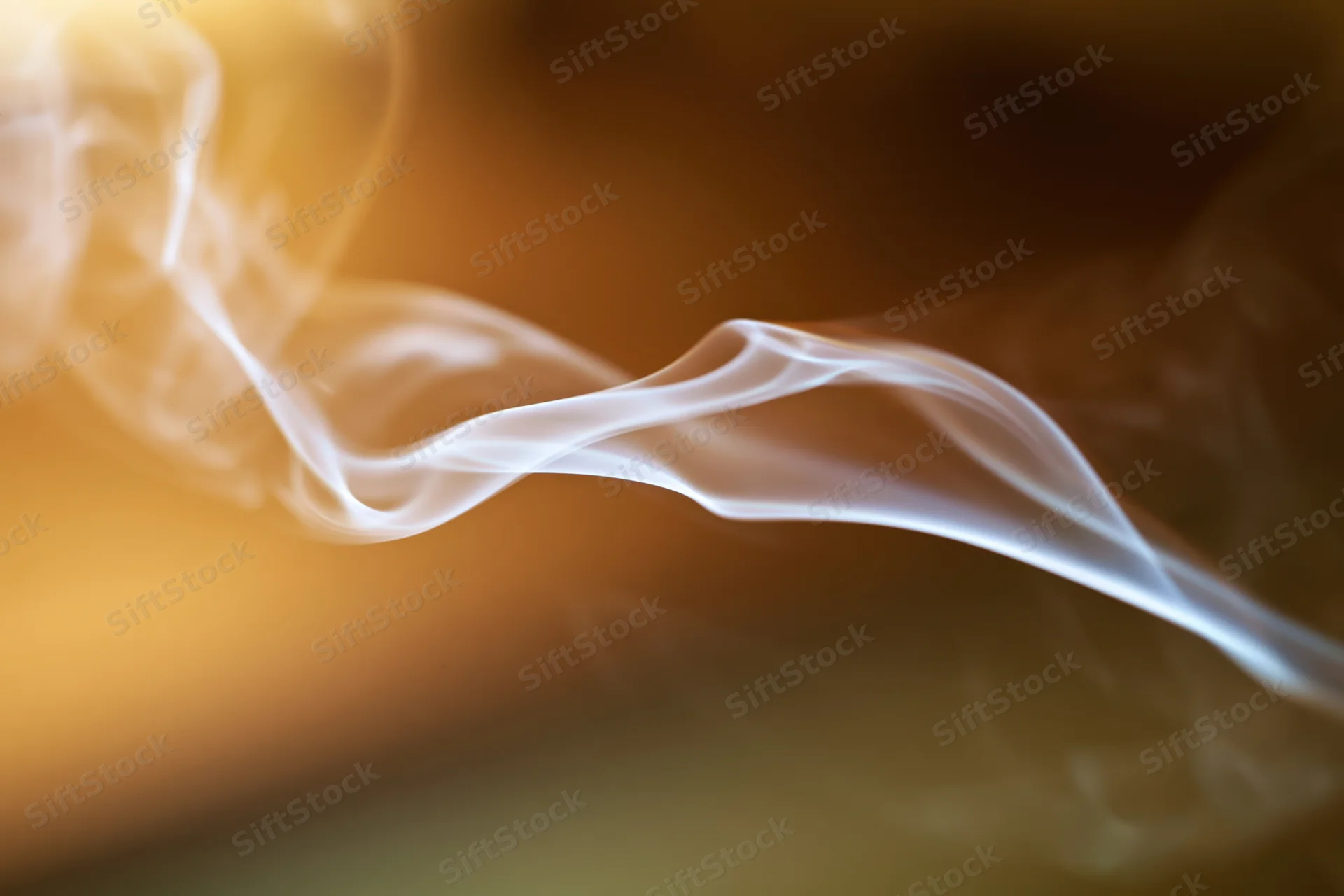 Wispy white smoke curling and drifting in thin tendrils against a warm blurred background