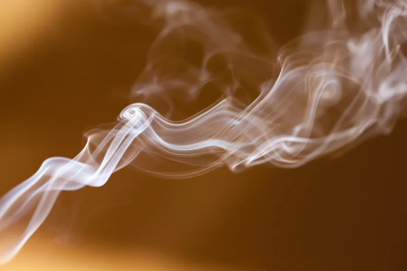 Wispy white smoke curling and drifting in thin tendrils against a warm golden background