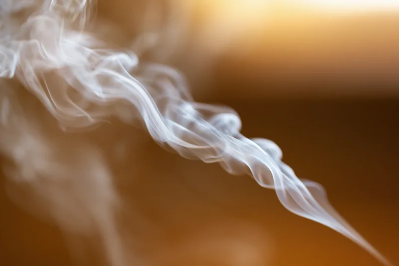 Wispy white smoke curling and drifting in thin tendrils against a warm blurred background