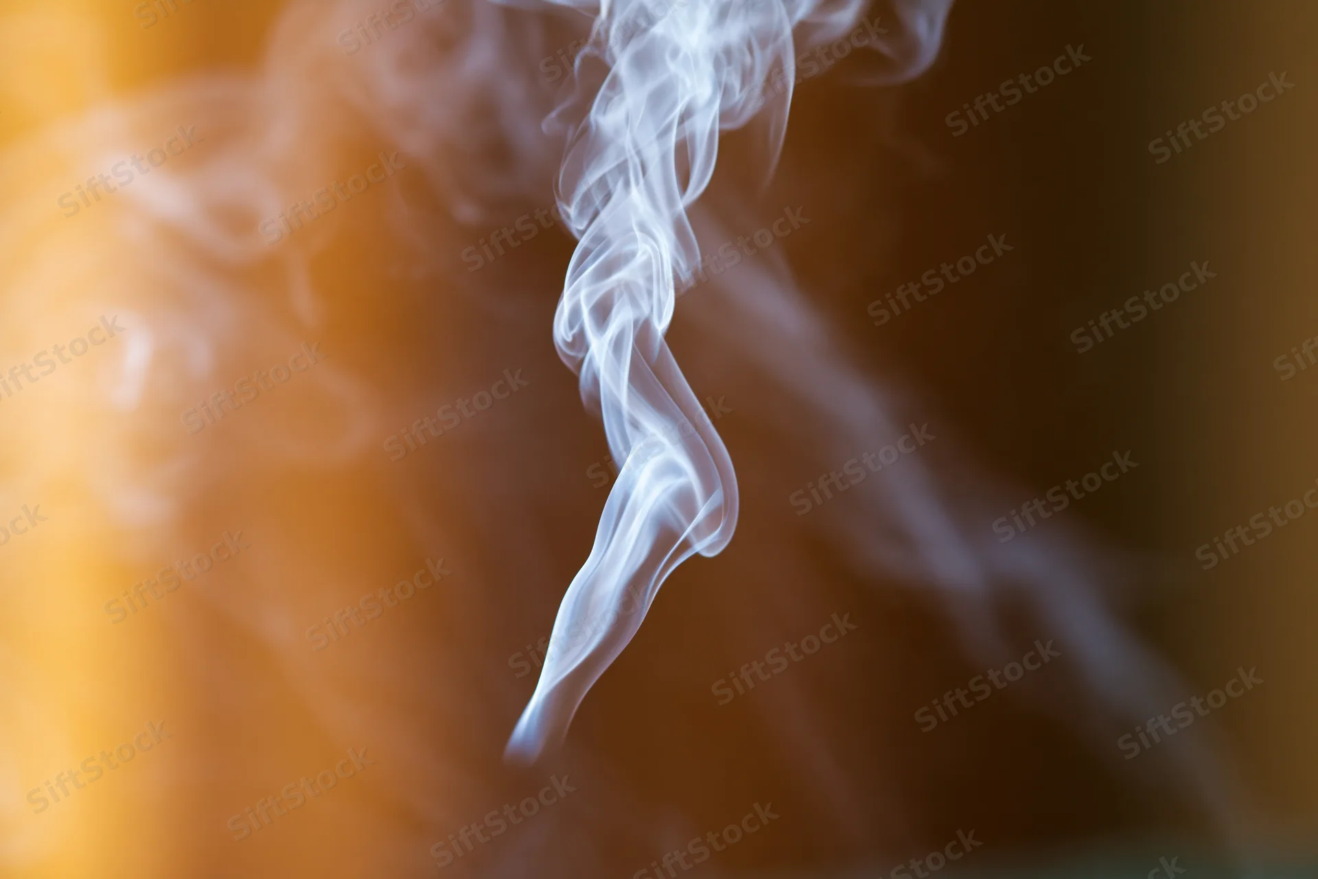 Wispy white smoke curling and drifting upward against a warm golden blurred background