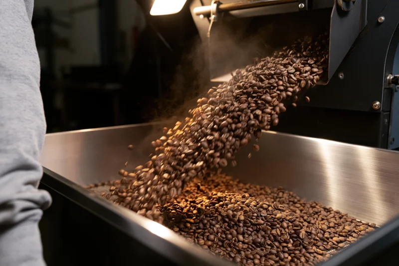 Coffee beans falling from roaster into metal tray in industrial setting