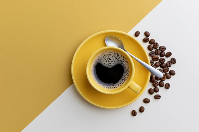 Yellow ceramic coffee cup with foam and beans on a white and yellow surface
