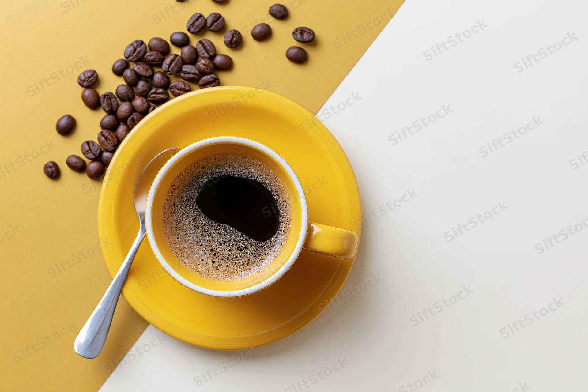 Yellow ceramic coffee cup with foam and beans on a two-tone surface
