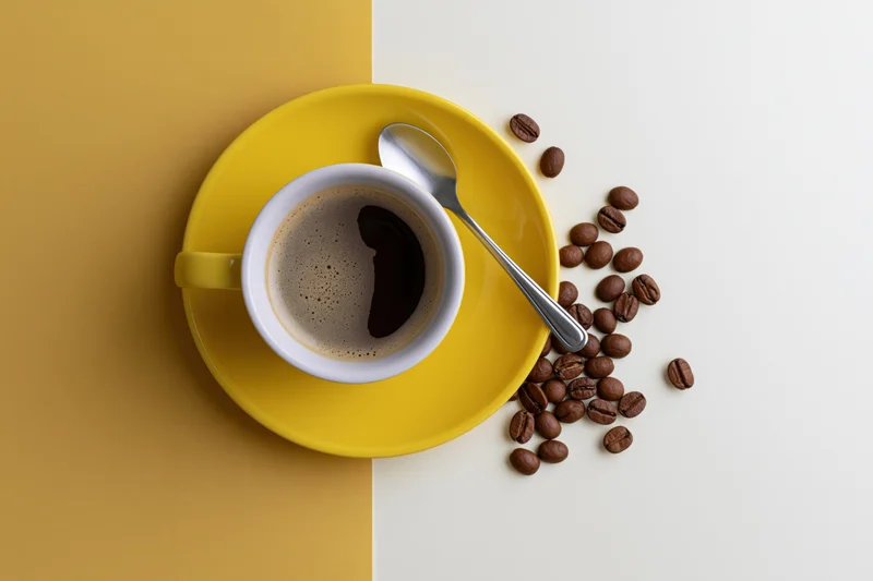 Yellow ceramic coffee cup with foam and scattered beans on a two-tone surface