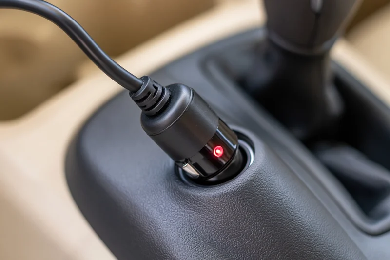 Black car charger adapter plugged into cigarette lighter socket in vehicle console
