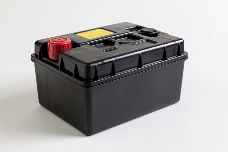 Black 12-volt car battery with red positive terminal on white background
