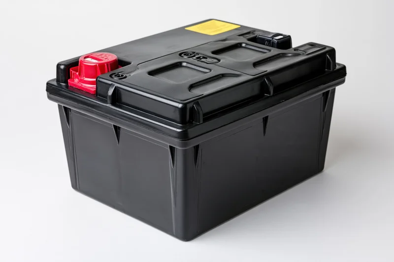 Black 12-volt car battery with red positive terminal on white background