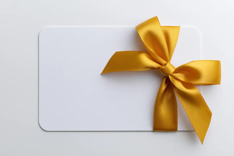 Blank white gift card with gold ribbon bow on plain background