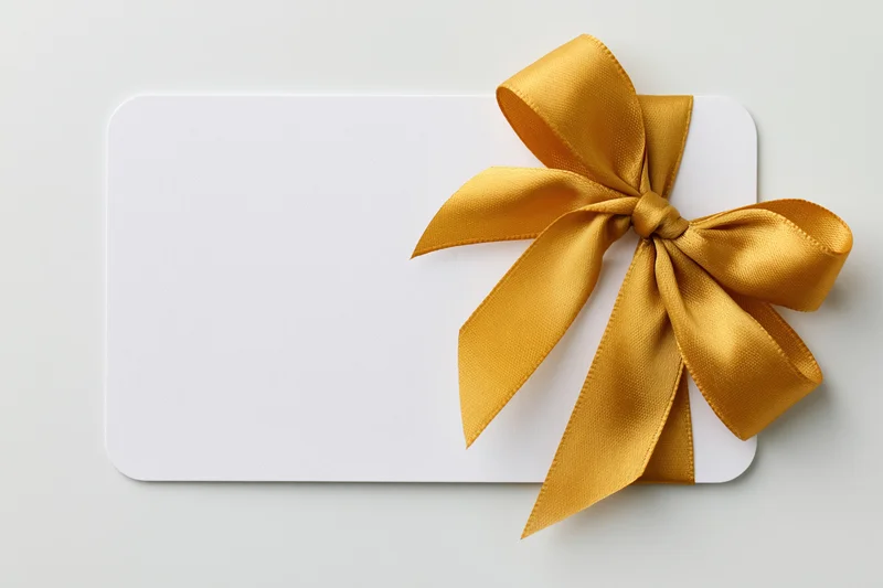 Blank white gift card with gold ribbon bow on light background