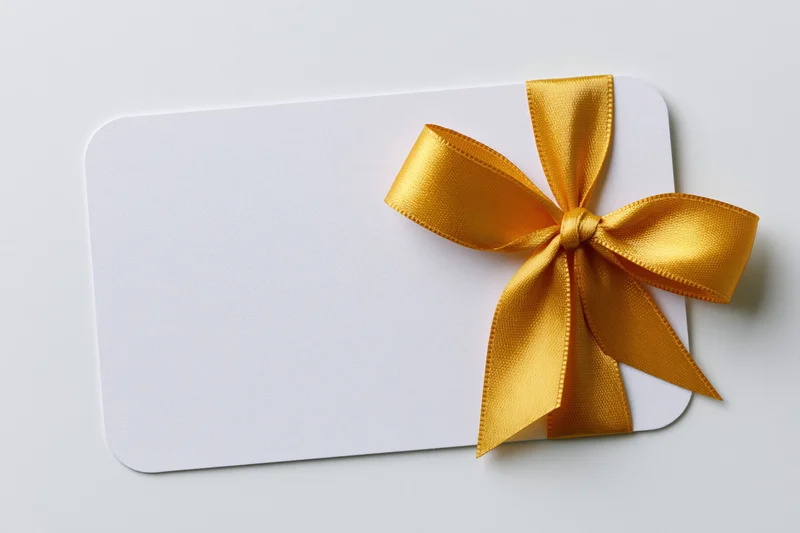 Blank white gift card with gold ribbon bow on plain background